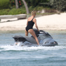 Charlize Theron wears a black one piece bikini as she hits the waves on a jet ski in Miami